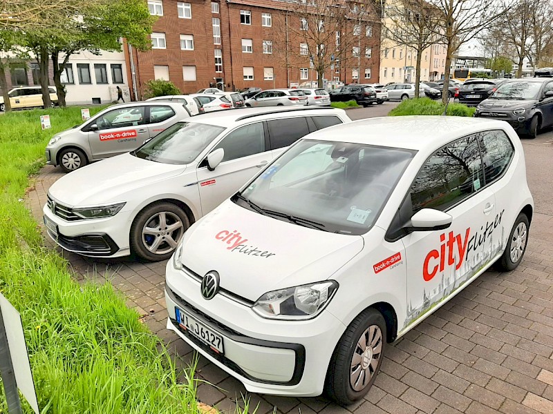 Ein Parkplatz in einer deutschen Stadt mit verschiedenen weißen book-n-drive-Fahrzeugen.
